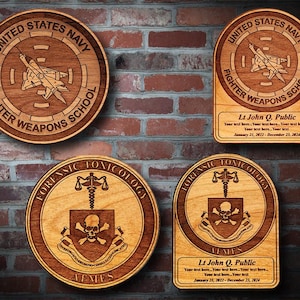 May include: Four wooden plaques with engraved designs. The top left plaque features a fighter jet and the text "UNITED STATES NAVY FIGHTER WEAPONS SCHOOL". The top right plaque features a fighter jet and the text "UNITED STATES NAVY FIGHTER WEAPONS SCHOOL". The bottom left plaque features a skull and crossbones and the text "FORENSIC TOXICOLOGY". The bottom right plaque features a skull and crossbones and the text "FORENSIC TOXICOLOGY".