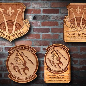 May include: Four wooden plaques with a military theme. The top plaque is a wing patch with the text "926th Wing" and dates "January 21, 2022 - December 23, 2025". The second plaque is a personalized plaque with the text "Lt John Q. Public" and dates "January 21, 2022 - December 23, 2025". The bottom two plaques are for a "Comm Support Squadron" with the text "Ctrl+Alt+Destroy" and dates "January 21, 2022 - December 23, 2025".