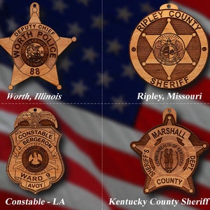 May include: Four wooden sheriff's badges with different designs. The top left badge is a five-pointed star with the text "DEPUTY CHIEF WORTH POLICE STATE OF ILLINOIS 88". The top right badge is a round badge with a five-pointed star and the text "RIPLEY COUNTY SHERIFF". The bottom left badge is a shield-shaped badge with the text "CONSTABLE J. BERGERON WARD 9 AVOY". The bottom right badge is a five-pointed star with the text "MARSHALL SHERIFF'S COMMONWEALTH OF KENTUCKY DEPT. COUNTY".