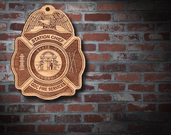 May include: Wooden plaque featuring a fire department emblem. The emblem includes an eagle, the words "Station Chief," and "State of Georgia." The plaque is brown and hangs against a brick wall. The text "GDC Fire Services" is also visible.