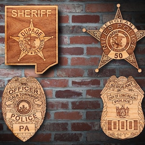 May include: Four wooden police badges with different designs and text. The top left badge is a sheriff's badge with the text "SHERIFF" and "DUPAGE COUNTY ILLINOIS". The top right badge is a star-shaped badge with the text "SERGEANT NILES STATE OF ILLINOIS POLICE 50". The bottom left badge is a round badge with the text "OFFICER CALN TOWNSHIP POLICE PA". The bottom right badge is a shield-shaped badge with the text "SERGEANT CITY OF LONG BEACH POLICE 000 N.Y."