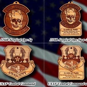 May include: Two wooden ornaments with a military theme. The first ornament is a brown and gold shield with the text "USAF CENT" and a globe design. The second ornament is a brown and gold shield with the text "316th SURGICAL OPS SO" and a skull design. Both ornaments have the text "ERIT SANGUIS" at the top.