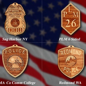 May include: Four wooden ornaments with different designs. The top left ornament is a brown and gold police badge with the text "Sag Harbor Police" and "000". The top right ornament is a brown six-sided shape with the text "LPM 26". The bottom left ornament is a brown shield-shaped ornament with the text "Police" and "Pima County Community College District". The bottom right ornament is a brown shield-shaped ornament with the text "Redmond Police" and "Est 1912".