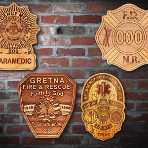 May include: Four wooden plaques with engraved designs. The top left plaque is a starburst shape with the words "Emergency Medical Services" and "Castle County" in a circle. The top right plaque is a fire department badge with the words "F.D." and "N.R." and the number "000". The bottom left plaque is a shield shape with the words "Gretna Fire & Rescue" and "Faith In God". The bottom right plaque is a starburst shape with the words "Emergency Medical Services" and "Austin-Travis County Texas".