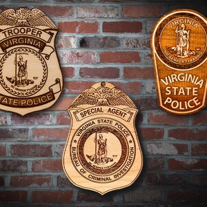 May include: Three wooden plaques with the Virginia State Police logo. The top plaque has the words "Virginia" and "State Police" in a banner around the logo. The middle plaque has the words "Special Agent" and "Bureau of Criminal Investigation" in a banner around the logo. The bottom plaque has the words "Virginia State Police" in a banner around the logo.