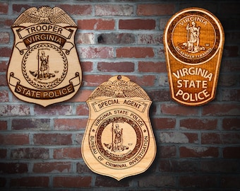 May include: Three wooden plaques with the Virginia State Police logo. The top plaque has the words "Virginia" and "State Police" in a banner around the logo. The middle plaque has the words "Special Agent" and "Bureau of Criminal Investigation" in a banner around the logo. The bottom plaque has the words "Virginia State Police" in a banner around the logo.