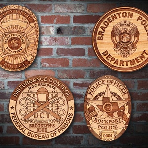 May include: Four wooden police badges with engraved designs. The badges are round and oval shaped with a brown wood finish. The badges feature the names of the police departments, including Palmetto Police Department, Bradenton Police Department, Disturbance Control Federal Bureau of Prisons, and Rockport Police.