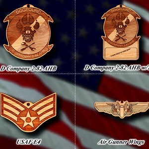 May include: Four wooden ornaments with different designs. The top left ornament is a circular design with the text "DOGPOUND" and "D COMPANY 2-82 AHB". The top right ornament is a similar circular design with the text "DOGPOUND" and "D COMPANY 2-82 AHB" with a blank space for text. The bottom left ornament is a wooden Air Force E4 rank insignia. The bottom right ornament is a wooden Air Gunner Wings insignia.