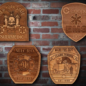 Könnte beinhalten: Vier Holzplaketten mit unterschiedlichen Designs. Die obere linke Plakette ist eine Plakette des New Yorker staatlichen Notfallsanitäters mit dem Staatssiegel und dem Text "New York State" und "Paramedic". Die obere rechte Plakette ist eine Cooper EMS-Plakette mit einem roten Lebensstern und dem Text "Cooper EMS". Die untere linke Plakette ist eine Micro Fire Dept-Plakette mit einem roten Kreuz und dem Text "Micro Fire Dept". Die untere rechte Plakette ist eine Micro Fire Dept-Plakette mit einem Dalmatiner und dem Text "Micro Fire Dept, Flame Tamers, Est. 1958".