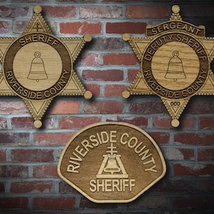 May include: Three wooden sheriff's badges with a bell and the text "Riverside County Sheriff" on each. The top two badges are star-shaped, and the bottom badge is a rounded rectangle.