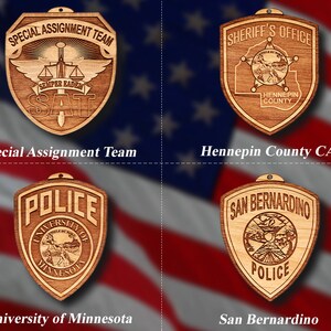 May include: Four wooden ornaments featuring different law enforcement designs. The top left ornament is a shield with the text "Special Assignment Team" and "SEMPER EADEM" with a sword and scales of justice. The top right ornament is a shield with the text "Sheriff's Office" and "Hennepin County". The bottom left ornament is a shield with the text "Police" and "University of Minnesota". The bottom right ornament is a shield with the text "San Bernardino Police".