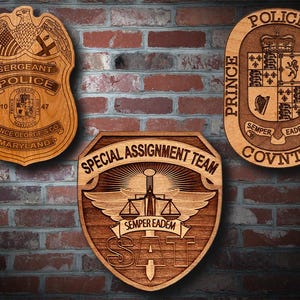 May include: Three wooden plaques with engraved designs. The top plaque is oval shaped and reads "Police George's County" with a coat of arms in the center. The left plaque is a traditional police badge with the text "Sergeant Police" and "Prince George's Co. Maryland". The right plaque is a shield shape with the text "Special Assignment Team" and "Semper Eadem".