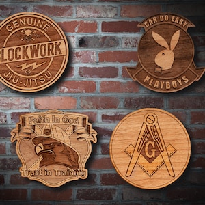 May include: Four wooden plaques with different designs. The top left plaque is brown with the text "GENUINE CLOCKWORK 09 JIU-JITSU". The top right plaque is brown with the text "CAN DO EASY PLAYBOYS" and a bunny rabbit silhouette. The bottom left plaque is brown with the text "Faith In God Trust in Training" and a stylized eagle head. The bottom right plaque is brown with a compass and square design and the letter "G" in the center.