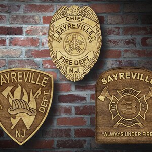 Könnte beinhalten: Drei Holzplaketten mit Sayreville Fire Department Logos. Die obere Plakette ist ein Abzeichen mit den Worten "Chief Sayreville Fire Dept. N.J.". Die linke Plakette ist ein Schild mit den Worten "Sayreville Fire Dept. NJ". Die rechte Plakette ist ein Quadrat mit den Worten "Sayreville Squad 3 Company" und "Always Under Fire".