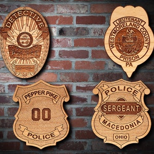 May include: Four wooden police badges with intricate engraved details. The badges include the words "Detective," "Police," "Sergeant," and various city names. The badges are displayed against a brick wall.