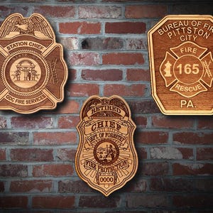 Könnte beinhalten: Drei Holzschilder mit eingravierten Designs. Eines trägt die Aufschrift "STATION CHIEF" mit "GDC FIRE SERVICES" und einem Siegel des Staates Georgia. Ein anderes lautet "BUREAU OF FIRE PITTSTON CITY" mit "FIRE 165 RESCUE PA." Das dritte lautet "RETIRED CHIEF DEPT OF FORESTRY FIRE PROTECTION".