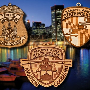 May include: Three wooden ornaments featuring the Maryland State Police logo. The first ornament is a traditional shield with the words "Maryland State Police" and the state flag. The second ornament is a shield with the words "Trooper Maryland State Police" and the state seal. The third ornament is a shield with the words "Maryland State Police Aviation Command" and a helicopter.