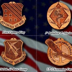 May include: Four wooden ornaments with different military unit insignia. The top left ornament features a shield with a winged design and the text "AUT VINCERE AUT MORI" and "First Fighter Wing". The top right ornament features a diamond shape with a dragon and sword design and the text "1st Battalion 4th Marines". The bottom left ornament features a shield with a winged design and the text "2849th Air Base Group". The bottom right ornament features a circle with a flying eagle and the text "VP-1 Screaming Eagles".