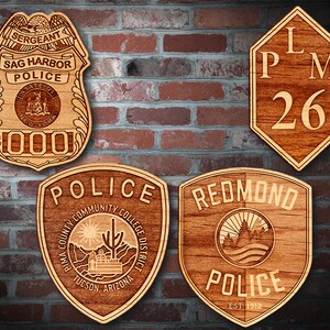 May include: Four wooden plaques with police department logos. The top left plaque is a brown and tan police badge with the text "Sag Harbor Police" and "Sergeant". The top right plaque is a brown and tan hexagon with the text "LPM 26". The bottom left plaque is a brown and tan shield with the text "Police" and "Pima County Community College District Tucson, Arizona". The bottom right plaque is a brown and tan shield with the text "Redmond Police Est. 1912".