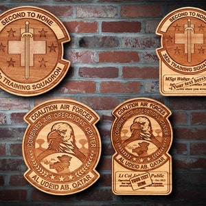 May include: Four wooden plaques with engraved designs. The top two plaques feature a sword and cross with the text "Second to None" and "382nd Training Squadron". The bottom two plaques feature an eagle and the text "Coalition Air Forces Combined Air Operations Center" and "Al Udeid AB, Qatar".