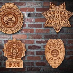 May include: Four wooden police badges on a brick wall. The top left badge is for the P.O.S.T. Commission of Nevada. The top right badge is for Truckee Police. The bottom left badge is for the Passaic County Prosecutors Office. The bottom right badge is for the Patrolman Napoleon of the Aux. Police.