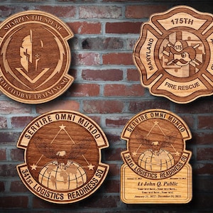 May include: Four wooden plaques with engraved designs. One features a spear and the text "SHARPEN THE SPEAR". Another is a fire rescue emblem with "175TH" and "MARYLAND AIR GUARD". The other two have an eagle and the text "SERVIRE OMNI MUNDO".