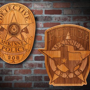 May include: Two wooden plaques with a police badge design. The left plaque is oval shaped and says "DETECTIVE MCKINNEY POLICE 208". The right plaque is shaped like a star and says "POLICE MCKINNEY TEXAS".