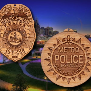May include: Two wooden ornaments featuring the Metropolitan Nashville Police Department logo. The first ornament is a traditional police badge with an eagle and the words "Metropolitan Police" and "Officer 000". The second ornament is a round design with a starburst and the words "Metro Police Nashville Davidson County".