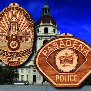 Könnte beinhalten: Zwei hölzerne Pasadena Police-Abzeichen. Eines ist oval, mit den Worten "LIEUTENANT" und "PASADENA POLICE" graviert. Das andere ist schildförmig mit "PASADENA POLICE" und einem Kronen-Design. Beide sind hellbraun.
