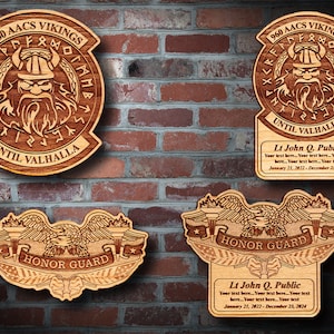 May include: Three wooden plaques with engraved designs. The top two plaques feature a Viking warrior with the text "960 AACS VIKINGS" and "UNTIL VALHALLA". The bottom plaque features an eagle with the text "HONOR GUARD". Each plaque has a personalized name and dates.