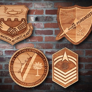 May include: Four wooden plaques with engraved designs. The top left plaque features a handshake and the text "Inter-American Air Forces Academy". The top right plaque features a shield with the text "778 Ever Foremost" and three stars. The bottom left plaque features a map of South Carolina with the text "USCG Base Charleston Supporting Coast Guard in the Low Country". The bottom right plaque features a star and three stripes with a globe design.