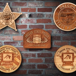 May include: Five wooden plaques with the Oregon State Police logo. The top plaque is a round plaque with the state seal. The other four plaques are rectangular and feature different units of the police department: Explosives Unit, Firearms Unit, and two more Firearms Unit plaques.