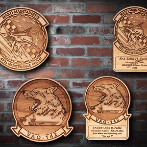 May include: Four wooden plaques with engraved designs. The top two plaques feature a shark with the text "MAKO MAINTAINERS" and "482D MAINTENANCE GROUP". The bottom two plaques feature a wolf with the text "VAQ-142".