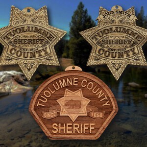 May include: Three wooden Tuolumne County Sheriff badges. Two are star-shaped, one with "John Smith" engraved. The third is a brown hexagon with a bear and the words "Tuolumne County Sheriff" and "Since 1850".