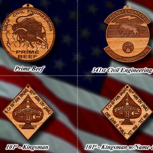 May include: Four wooden ornaments with different designs. The top left ornament is round and features a bull with the text "USAF CIVIL ENGINEERING PRIME BEEF". The top right ornament is round and features a bison with the text "BIG SKY ENGINEERS 341st CIVIL ENGINEERING SQ". The bottom left ornament is diamond shaped and features a spade with the text "B Co 101st AVN BN(AH) 101st ABN DIV (AML) OPERA NON VERBA KINGSMAN". The bottom right ornament is diamond shaped and features a spade with the text "B Co 101st AVN BN(AH) 101st ABN DIV (AML) OPERANONVERBA KINGSMAN CW2 JOHN Q. PUBLIC TET 1968-TET 1969".