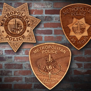 May include: Three wooden plaques with the Las Vegas Metropolitan Police Department logo. The first plaque is a star shape with the words "Metropolitan Police" and "Las Vegas" in a circle around a cityscape. The second plaque is a shield shape with the words "Metropolitan Police" and "Las Vegas" in a circle around a cityscape. The third plaque is a shield shape with the words "Metropolitan Police" and "Las Vegas Gang Unit" around a snake with a sword.