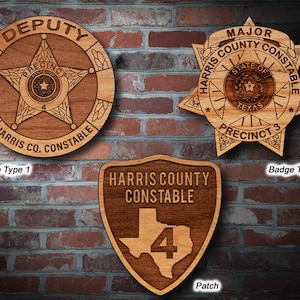 May include: Three wooden plaques with different designs for the Harris County Constable. The first plaque is a round badge with a star and the text "DEPUTY PRECINC 4 HARRIS CO. CONSTABLE". The second plaque is a star-shaped badge with the text "MAJOR HARRIS COUNTY CONSTABLE STATE OF TEXAS PRECINCT 3". The third plaque is a shield-shaped patch with the text "HARRIS COUNTY CONSTABLE" and the number "4" inside a Texas outline.