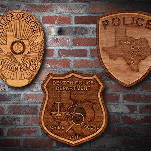 May include: Three wooden police badges with the text "Police Officer", "Police", and "Denton Police Department". The badges are all in the shape of a shield and feature the state of Texas.