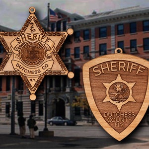 May include: Two wooden sheriff's badges. The first badge is a five-pointed star with the words "Sheriff, State of New York, Dutchess Co., N.Y." The second badge is a shield shape with the words "Sheriff, Dutchess County, N.Y."