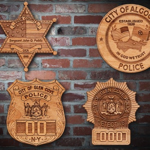 May include: Four wooden police badges with intricate designs, mounted on a brick wall. The badges include a star-shaped sheriff's badge, a circular badge with flags, and two shield-shaped badges. Each badge features text such as "Police" and "Detective".