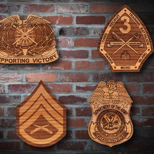 May include: Four wooden plaques with military insignia. The top left plaque features a winged eagle with a wheel and crossed keys, and the text "SUPPORTING VICTORY". The top right plaque is a shield with the text "THIRD RECRUIT TRAINING BATTALION", "SPIRIT", "DISCIPLINE", "PARRIS ISLAND", "MCRD", and the number "3". The bottom left plaque is a chevron with crossed rifles. The bottom right plaque features a shield with an eagle and the text "DEPARTMENT OF THE ARMY", "CRIMINAL INVESTIGATION COMMAND", "CID AGENT".