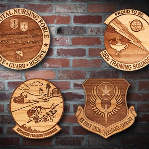 May include: Four wooden plaques with laser-engraved designs. The top left plaque is round and reads "USAF TOTAL NURSING FORCE" with a nursing symbol and the text "Thank you for taking care of us, perhaps you realize what it means. SMSgt John Q. Public." The top right plaque is round and reads "PROUD TO BE 383D TRAINING SQUADRON" with a lightning bolt, a lamp, and a globe. The bottom left plaque is round and reads "ADVANCED TRAINING PROGRAMS" with a cartoon airplane. The bottom right plaque is shaped like a shield and reads "AIR FORCE SPECIAL OPERATIONS COMMAND" with a star, wings, and a sword.