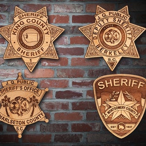 May include: Four wooden sheriff's badges with different designs and text. The top left badge says "King County Sheriff" with the state of Washington inside. The top right badge says "Deputy Sheriff Berkeley S.C." The bottom left badge says "J.Q. Public Sheriff's Office Charleston County S.C." The bottom right badge says "Sheriff Montgomery County Est. 1837".