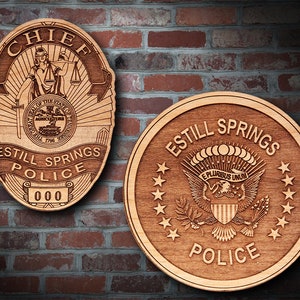 May include: Two wooden plaques with the words "Chief" and "Estill Springs Police" engraved on them. The "Chief" plaque features a stylised image of a woman holding scales of justice. The "Estill Springs Police" plaque features a stylised image of the Great Seal of the United States.