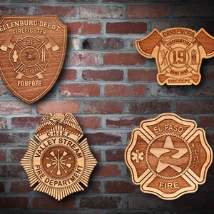 May include: Four wooden plaques with different firefighter department logos. The top left plaque is a shield shape with the text "Ellenburg Depot Firefighter 21 Est 1947 Poupore". The top right plaque is a red and white shield with the text "Dannemora Firefighters 19 Name Here Fire Dept.". The bottom left plaque is a round badge with the text "Chief Valley Stream Fire Department". The bottom right plaque is a four-pointed star with the text "El Paso Fire".
