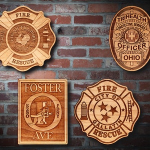 May include: Four wooden plaques with different designs. The top left plaque is a fire department badge with the text "FIRE CITY OF FILLMORE CALIFORNIA RESCUE". The top right plaque is a badge with the text "TRIHEALTH PROTECTIVE SERVICES OFFICER OHIO". The bottom left plaque is a rectangular plaque with the text "FOSTER E250 FDNY AVE". The bottom right plaque is a fire department badge with the text "FIRE CITY OF GALLATIN RESCUE".