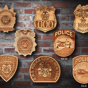 May include: A collection of eight wooden police badges with different titles and designs. The badges are all in a similar style, with a gold-colored background and black lettering. The badges are arranged in a grid pattern on a brick wall.