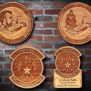 Könnte beinhalten: Vier Holzplaketten mit gravierten Designs. Die beiden oberen Plaketten zeigen den Text "USS Abraham Lincoln CVN 72" und "Shall Not Perish". Die beiden unteren Plaketten zeigen den Text "Find A Way" und "794th Communications Sq".