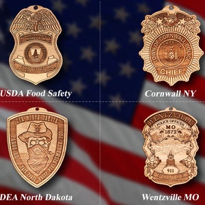 May include: Four wooden ornaments featuring different law enforcement agencies. The top left ornament is a USDA Food Safety Inspector badge. The top right ornament is a Town of Cornwall Police Chief badge. The bottom left ornament is a DEA North Dakota badge. The bottom right ornament is a Wentzville, MO Police Officer badge.
