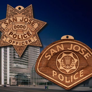 May include: Two wooden ornaments shaped like police badges. The first badge is a six-pointed star with the words "San Jose Police Officer" and "0000" in the center. The second badge is a rounded rectangle with the words "San Jose Police" in the center.
